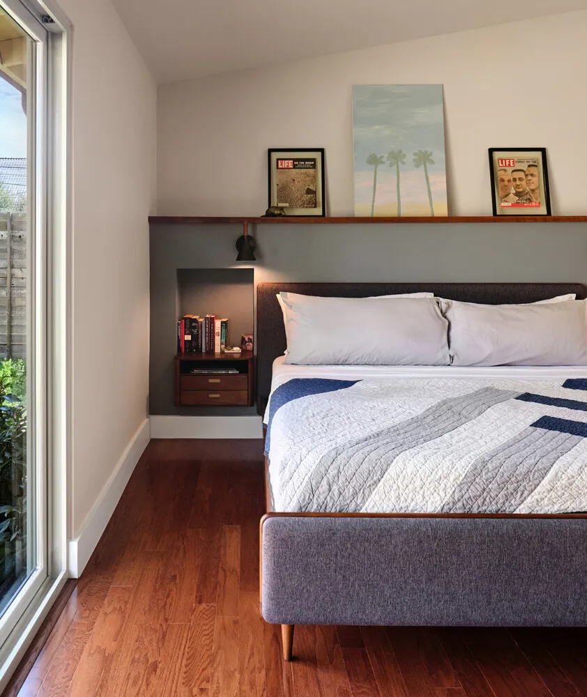 Bed against a white wall with a floating shelf and wall sconces