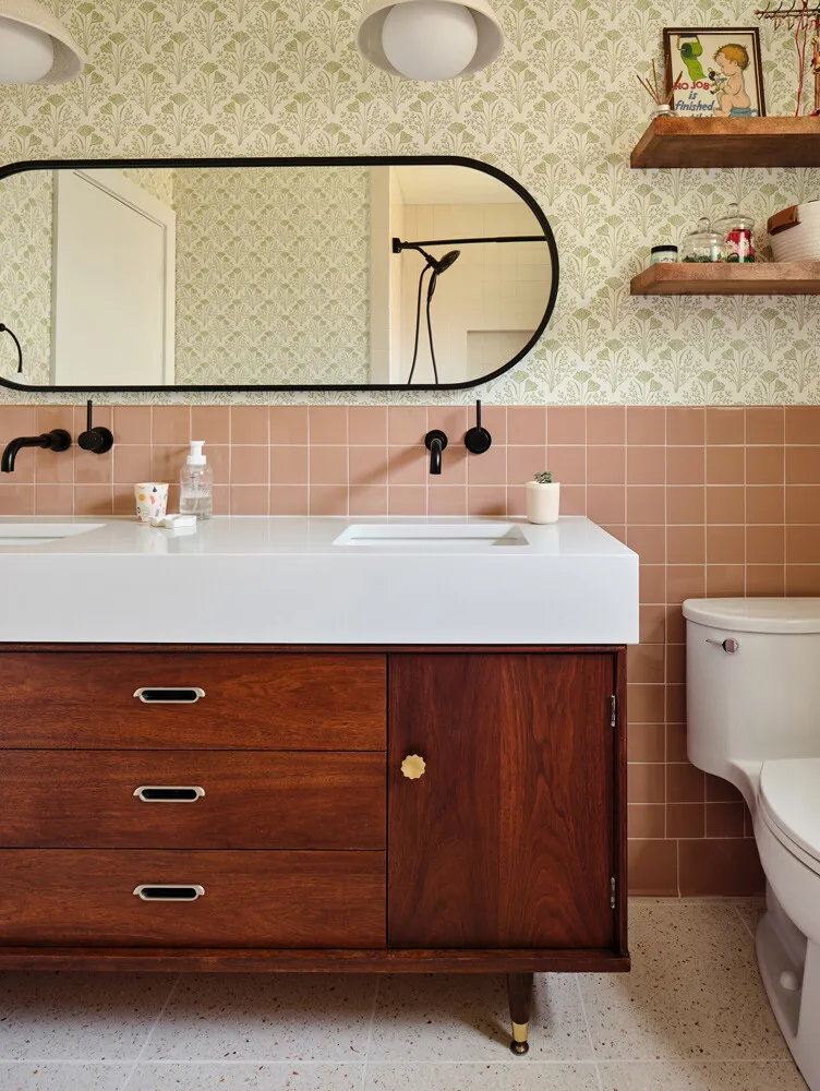 Walnut vanity with brass pulls below a long black-framed mirror