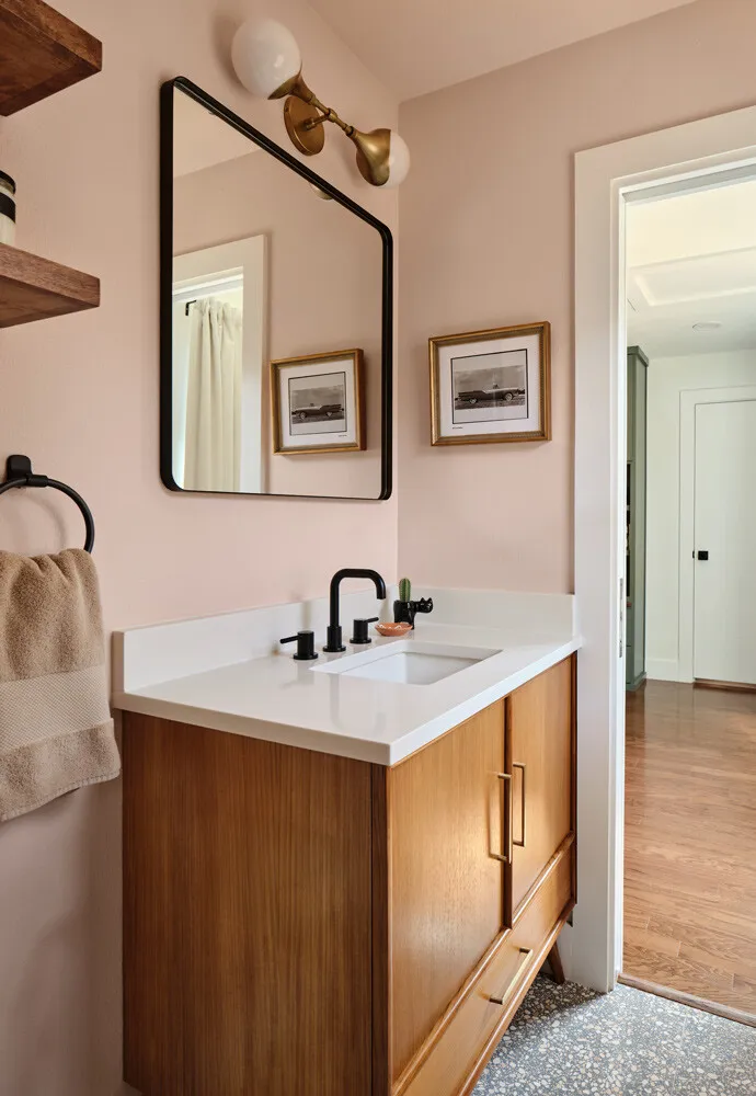 Wood vanity with a white top below a black-framed mirror