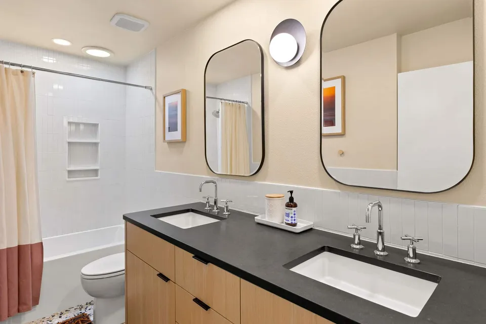 Double vanity with a black counter and chrome faucets below rounded mirrors