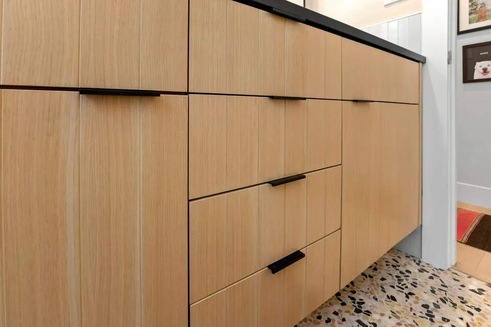 Flat-panel white oak vanity drawers with black pulls above a terrazzo floor
