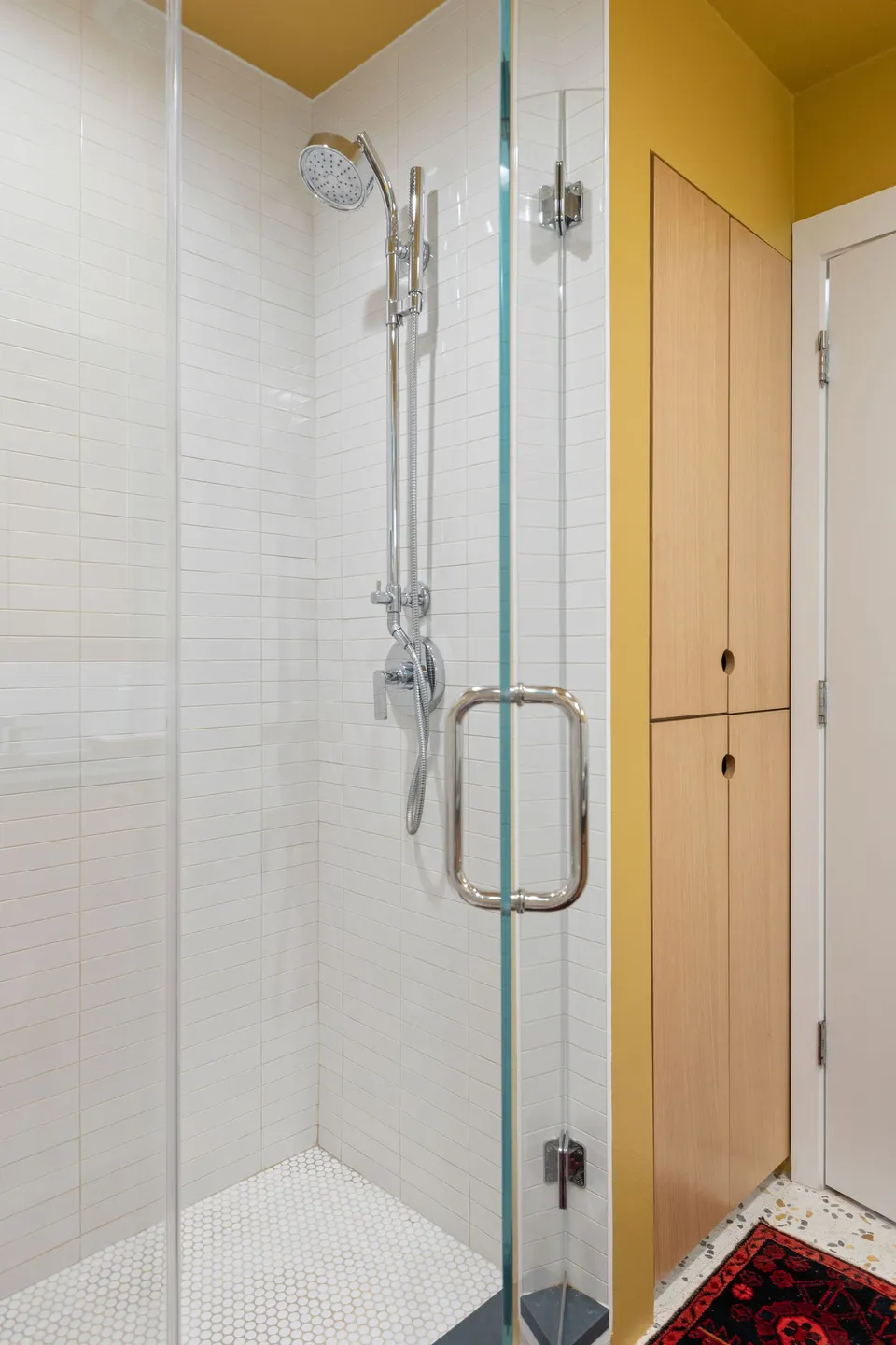 Glass shower with white tile and a tall white oak linen cabinet