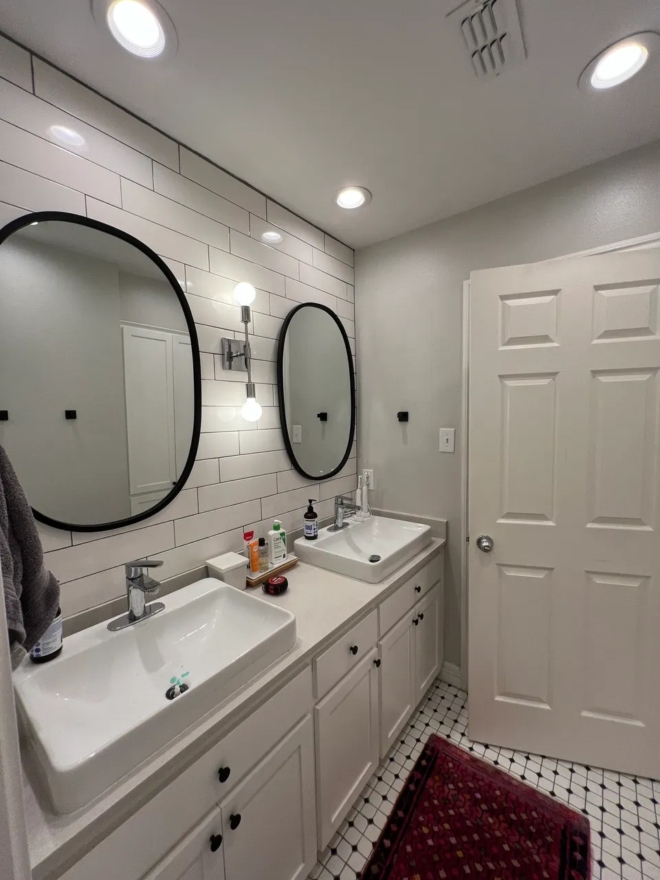 Hall bath before the remodel, with a white double vanity, oval mirrors and a black and white tile floor