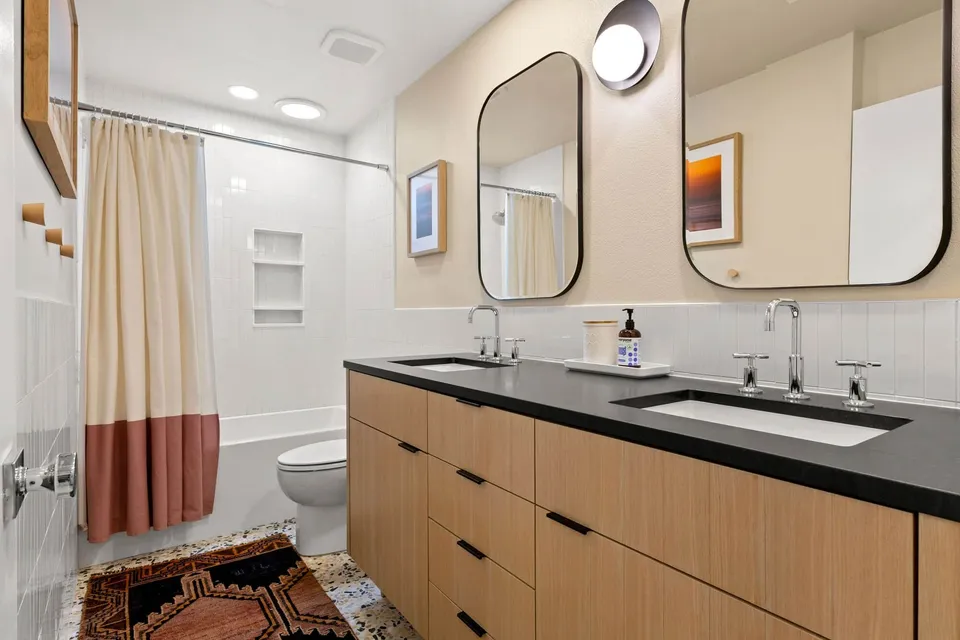 Hall bath with a white oak double vanity, a black counter and a tub with a striped curtain