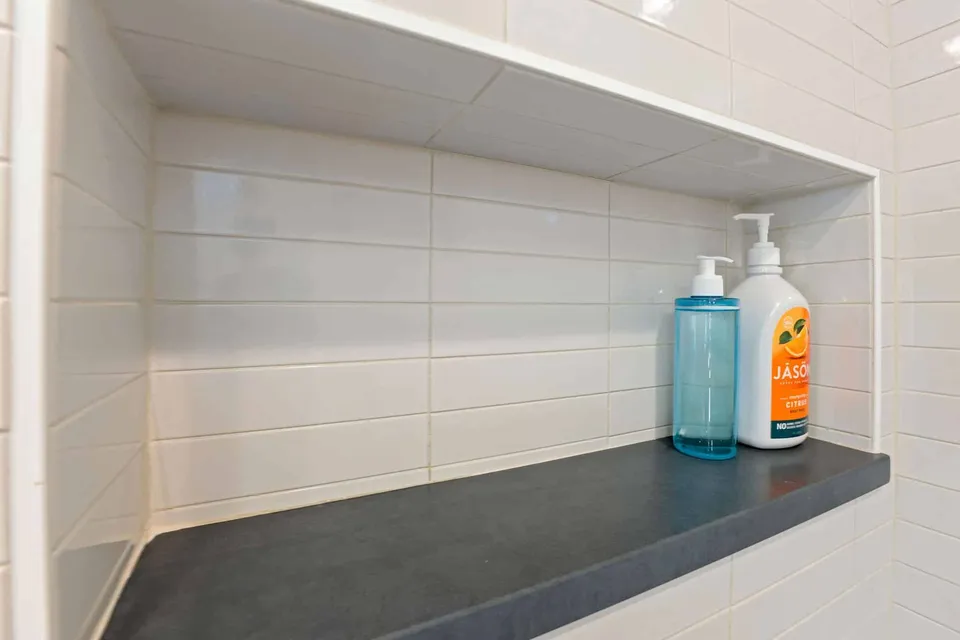 Long shower niche with white tile and a black stone shelf