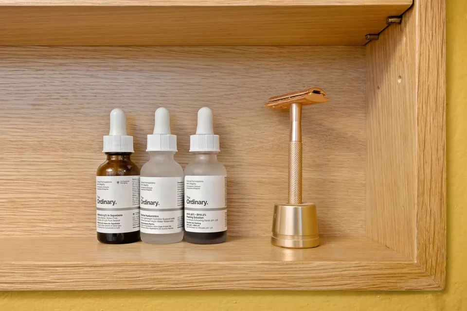 Recessed white oak niche with skincare bottles and a brass razor