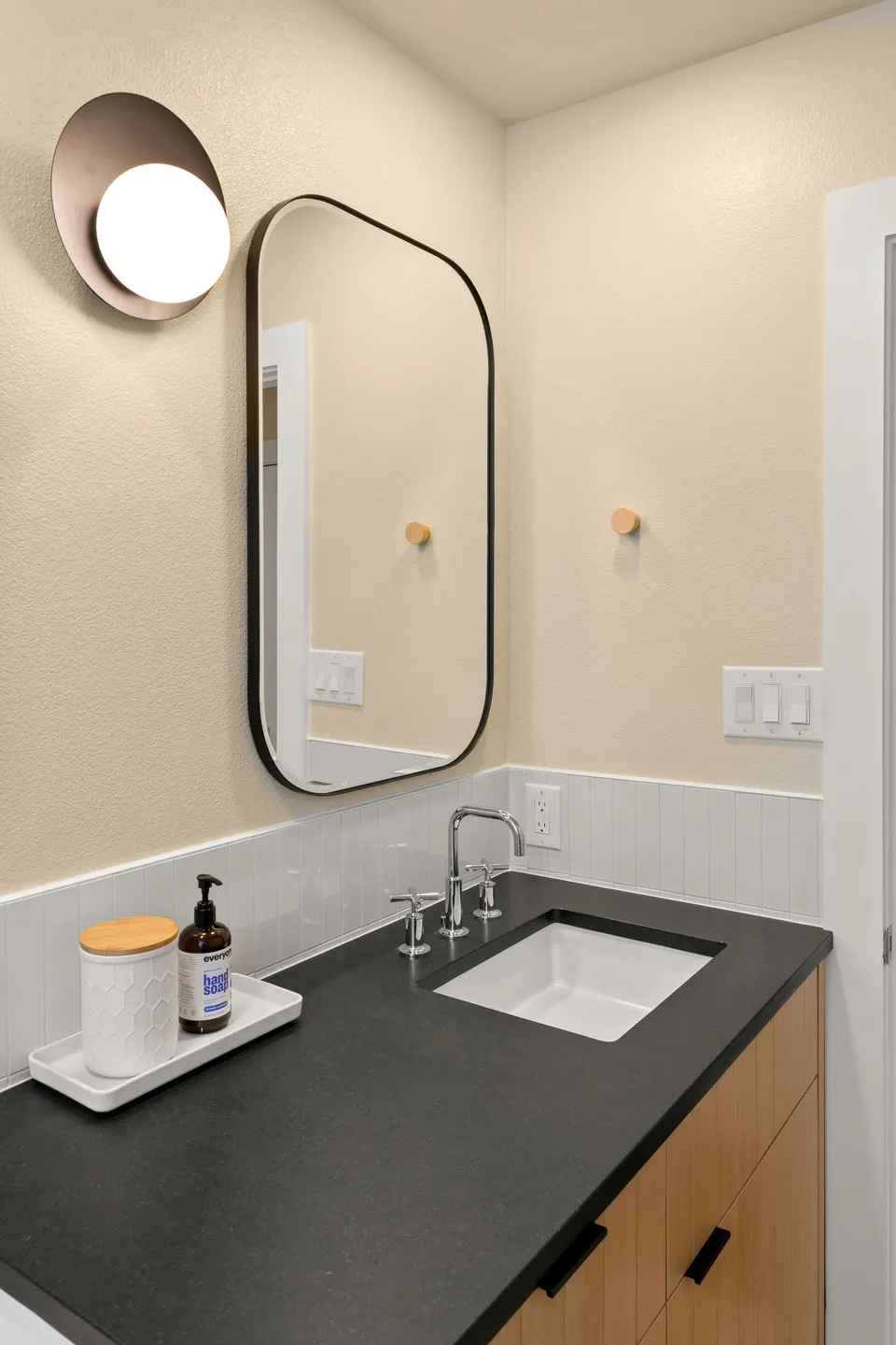 Rounded black mirror and a globe sconce above a black counter and chrome faucet