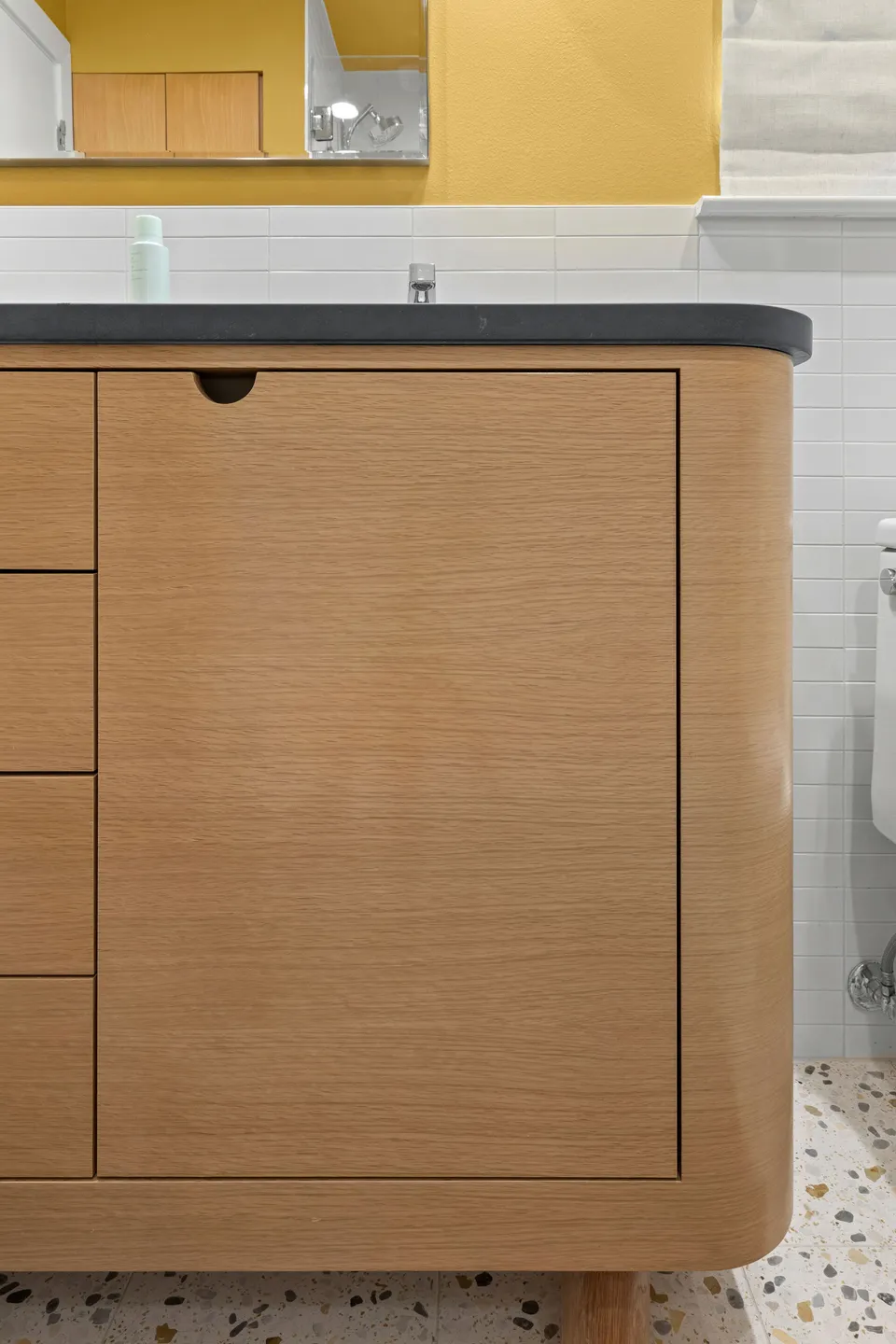 Rounded corner of a white oak vanity on a terrazzo floor