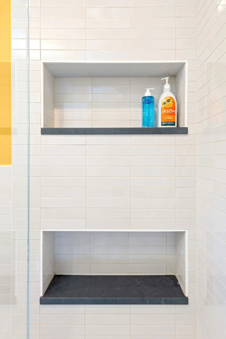 Shower with white tile and two niches with black stone shelves