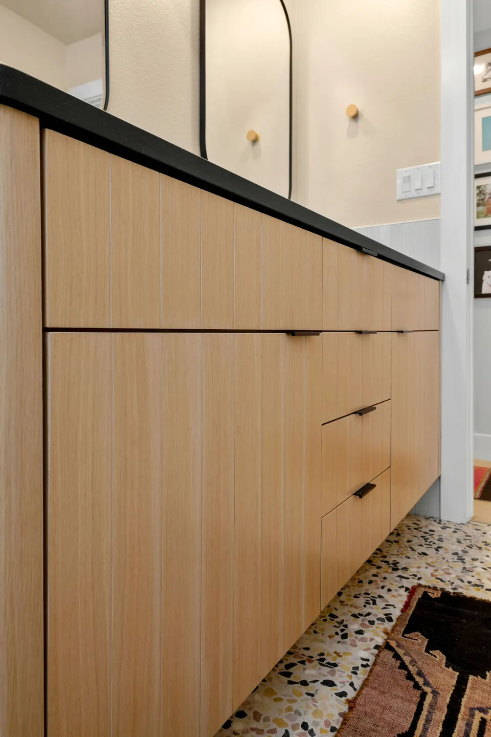 Side of the white oak vanity with a black counter on a terrazzo floor