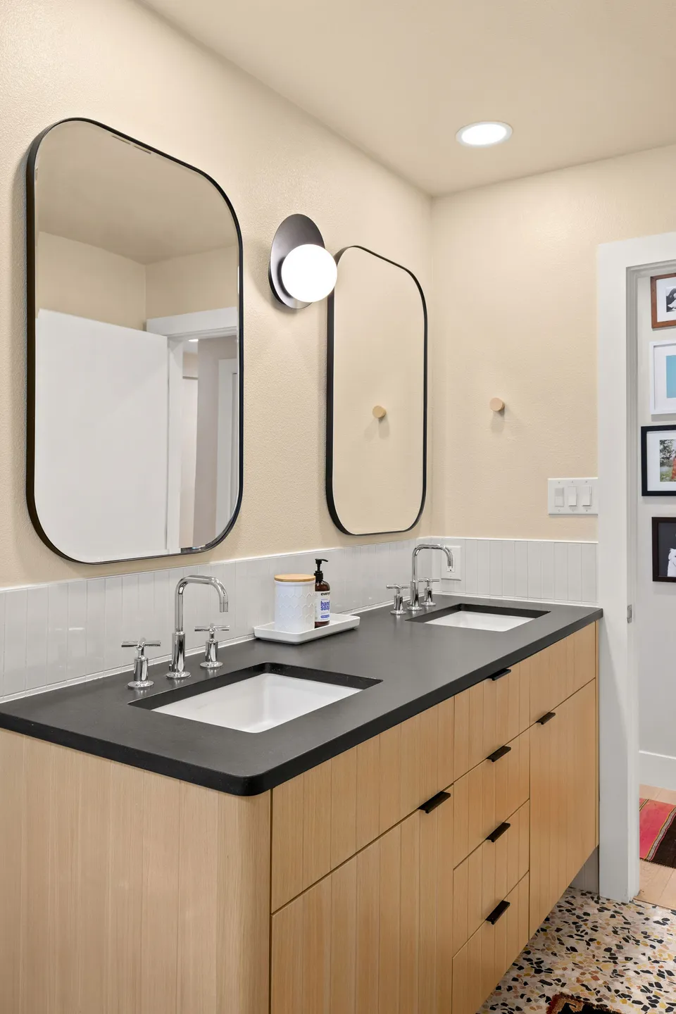 Hall bath after the remodel, with a white oak vanity, a black counter and rounded black mirrors