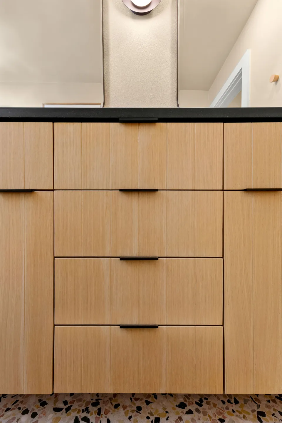 White oak vanity drawers with black pulls below a black counter