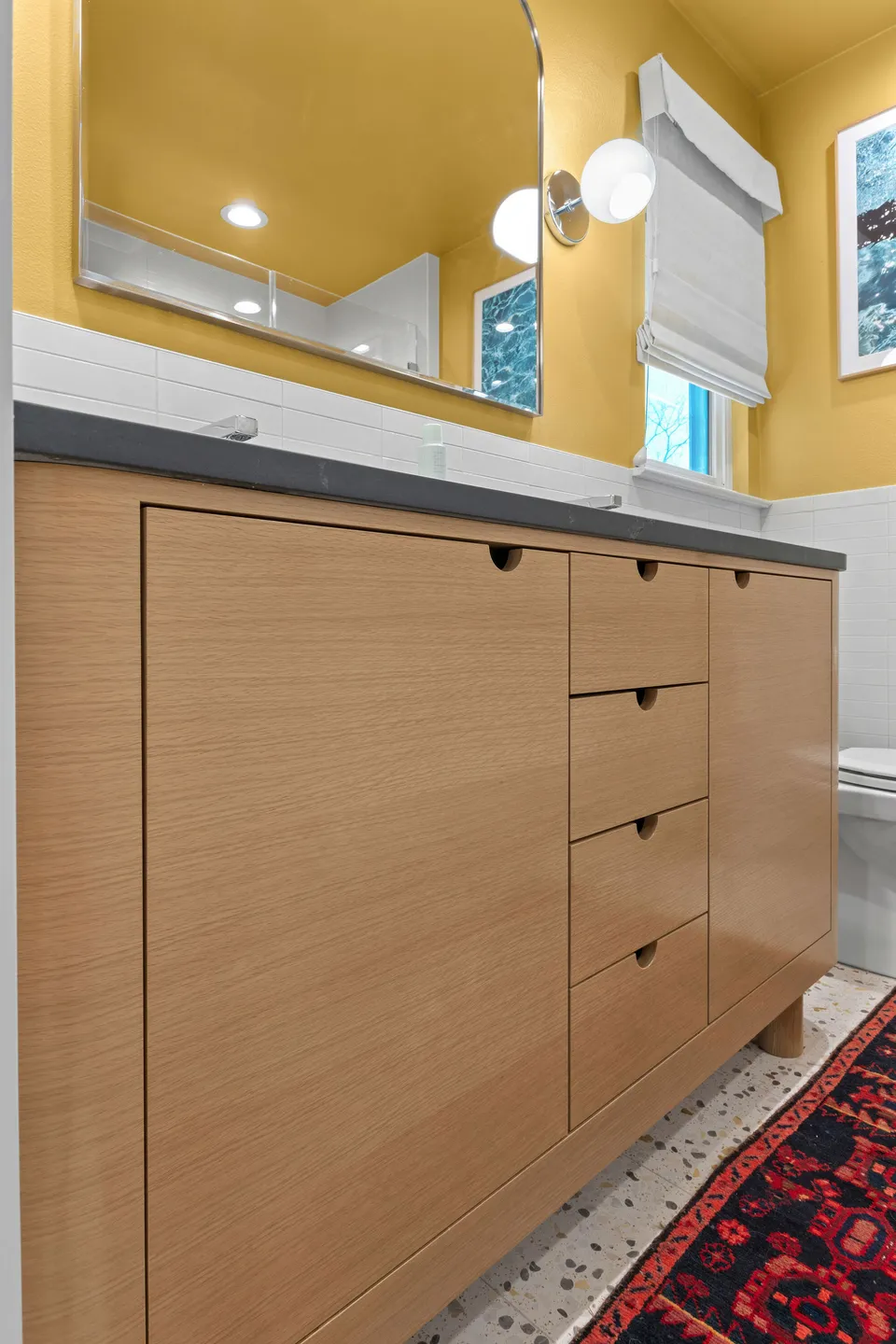 White oak vanity with drawers, a grey counter and a red rug