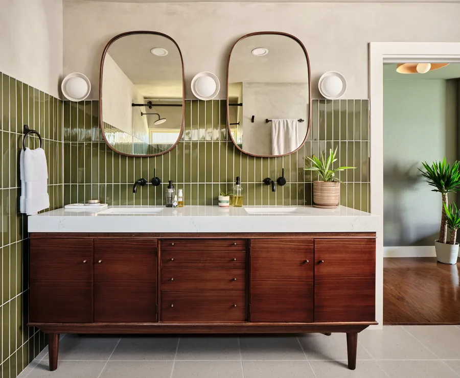 Mid-century walnut double vanity with green vertical tile and two oval mirrors