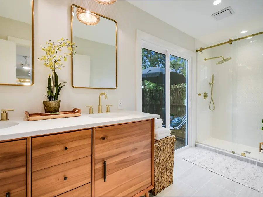 Bathroom with a wood double vanity, brass mirrors, and a glass shower