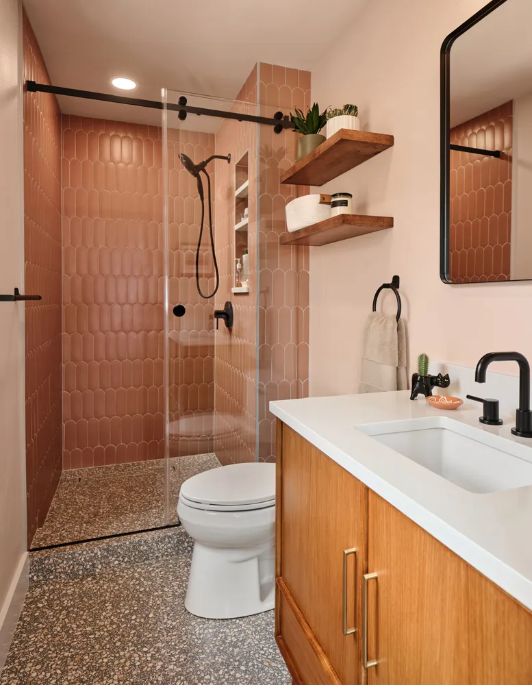 Walk-in shower with terracotta tile and a glass panel beside a wood vanity on a terrazzo floor