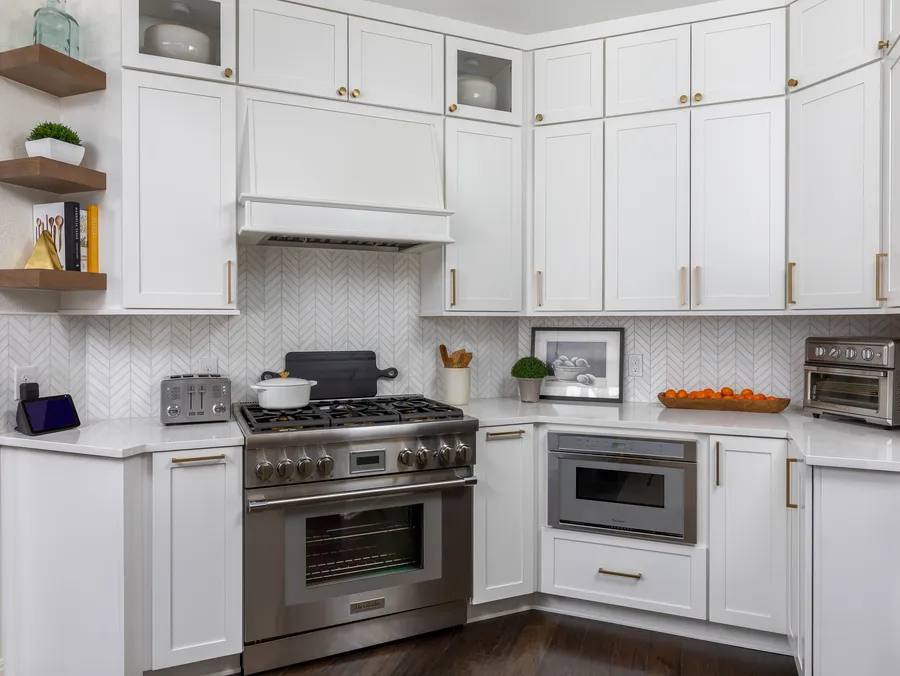 White shaker cabinets with brass pulls around a stainless range and herringbone backsplash