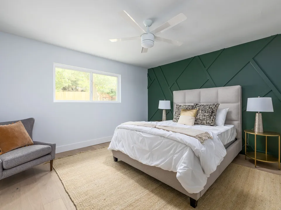 Bedroom with a green geometric accent wall and an upholstered bed