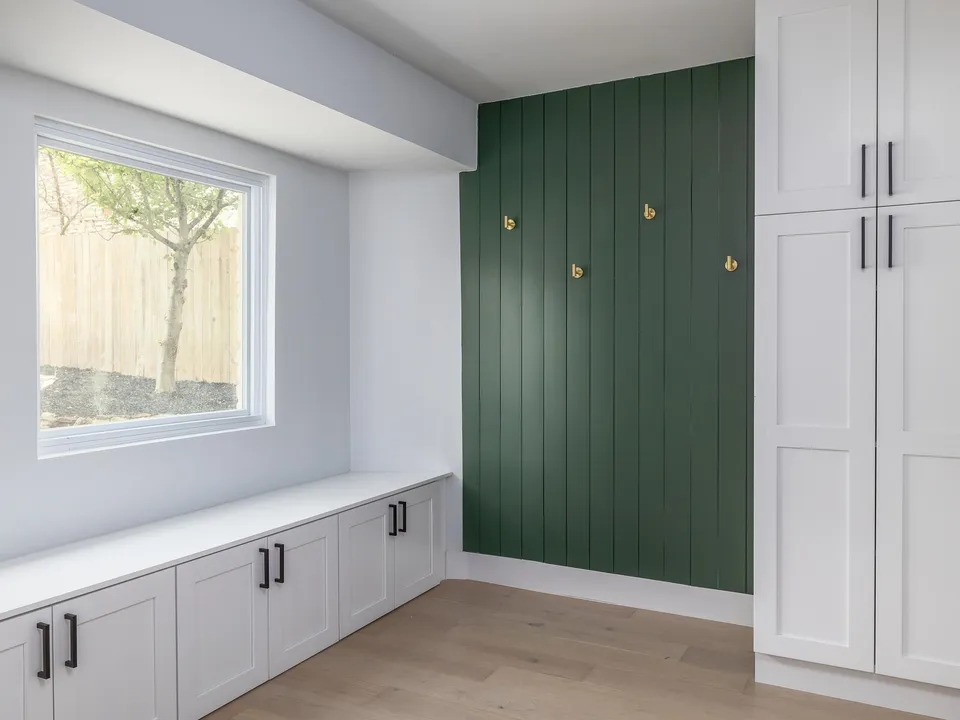 Breakfast nook with white cabinets and a green board and batten wall with brass hooks