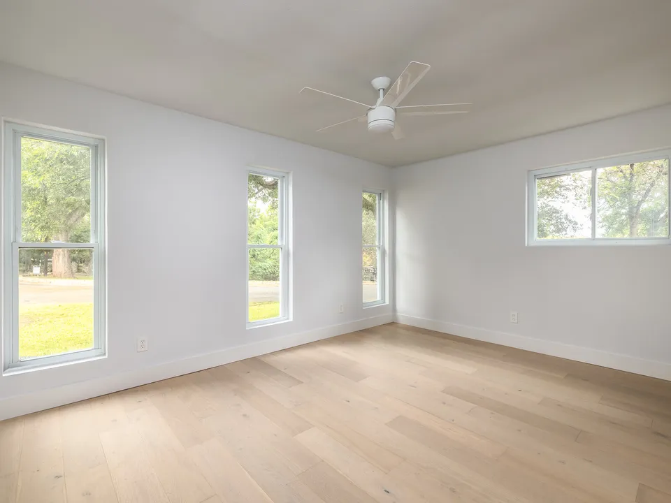 Empty bedroom with three windows and light oak floors