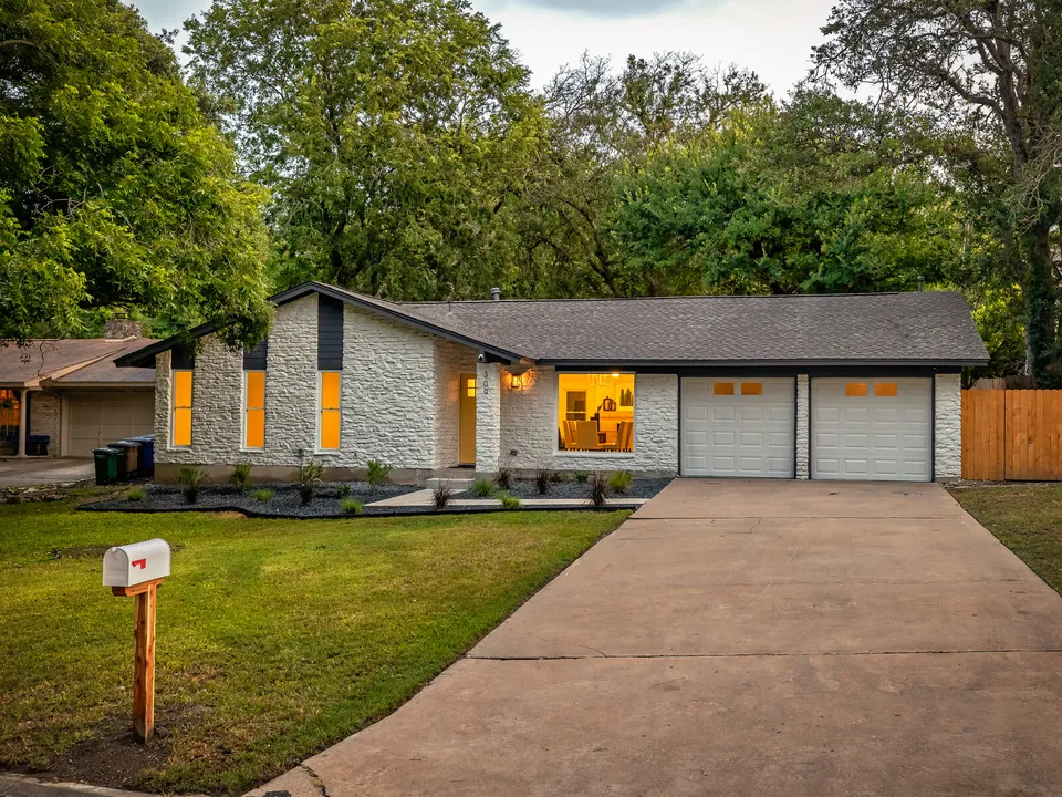 Front of the white stone ranch house at dusk with a two-car garage
