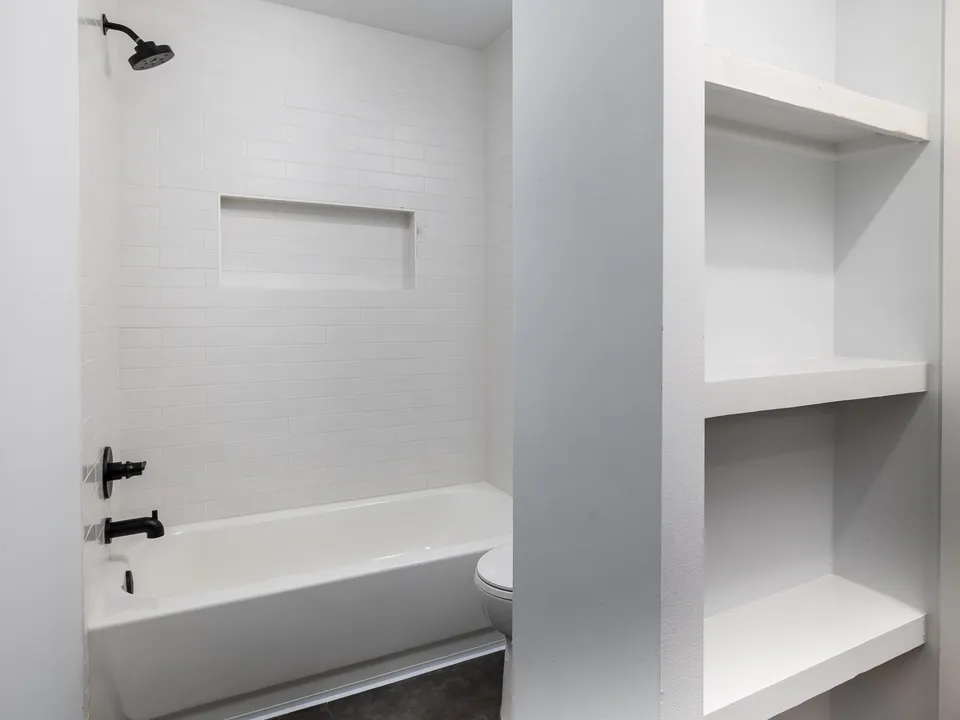 Hall bath with white subway tile, a tub, black fixtures and built-in shelves