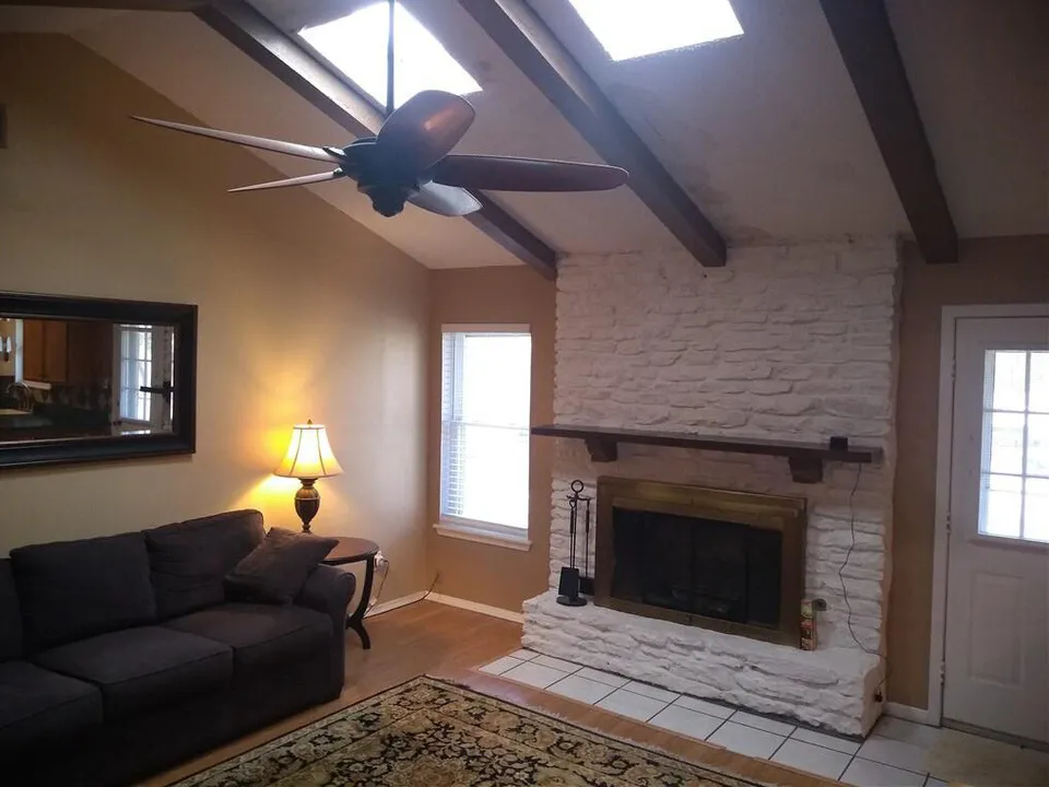 Living room before the remodel, with dark beams, a white stone fireplace and a brown sofa
