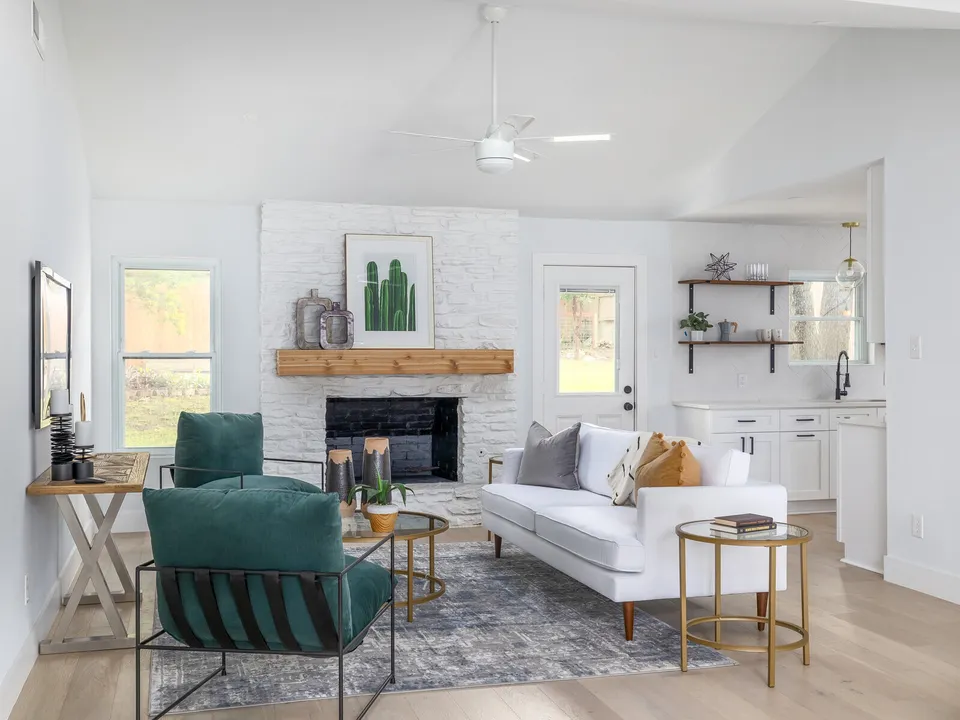Living room after the remodel, with a painted brick fireplace, a white sofa and green chairs