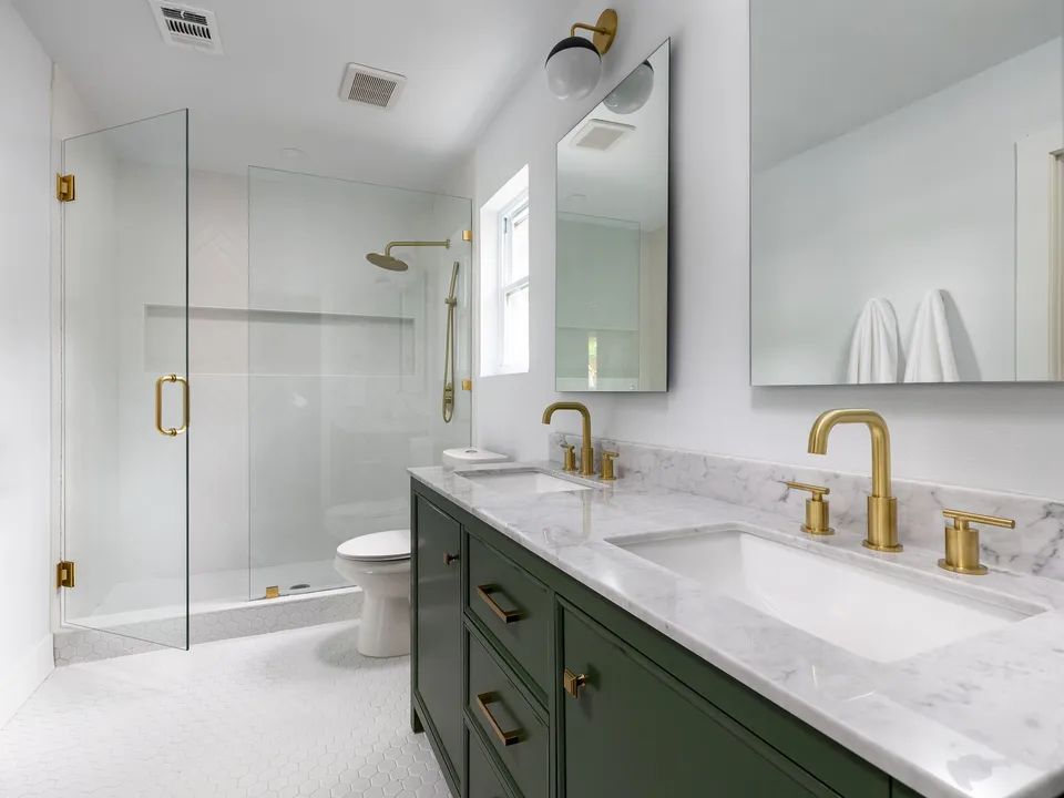Primary bath with a green double vanity, brass fixtures and a glass shower
