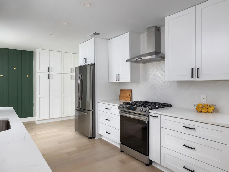 White shaker kitchen with herringbone tile, a stainless range and a green pantry wall