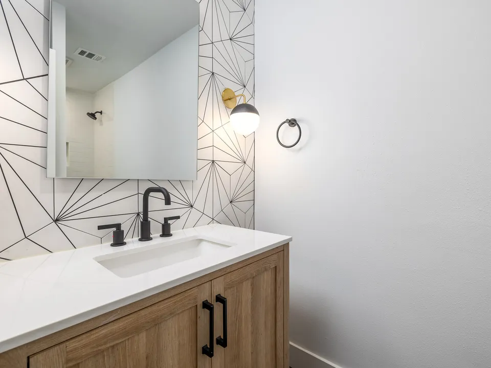 Wood vanity with black fixtures on a white and black geometric tile wall