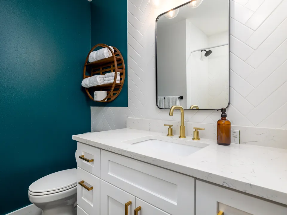Bathroom with a teal accent wall, a white shaker vanity and brass fixtures