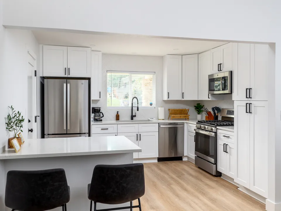 Kitchen with a white island, black bar stools and stainless appliances