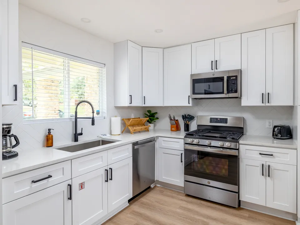 White shaker kitchen with a black faucet, a gas range and a microwave above