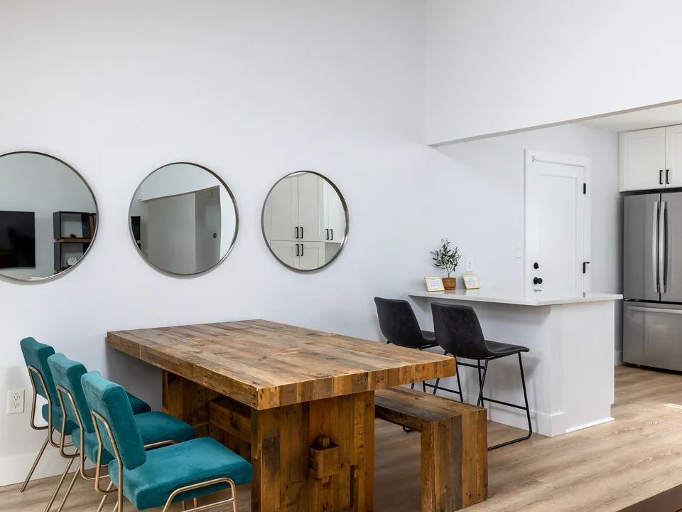 Wood dining table with teal chairs beside a white peninsula