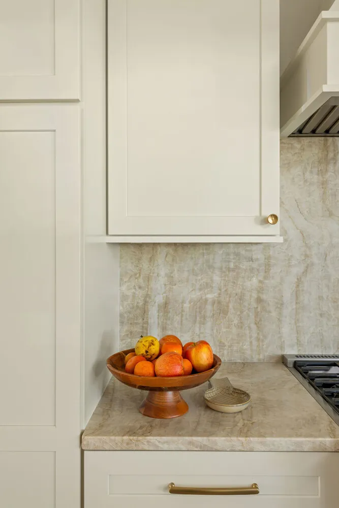 Cream cabinets and a quartzite backsplash with a bowl of oranges on the counter