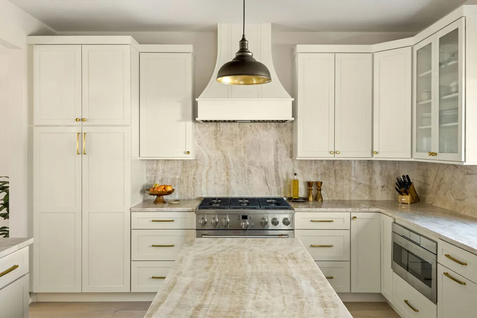 Kitchen after the remodel, with cream shaker cabinets, a plaster hood and a quartzite backsplash