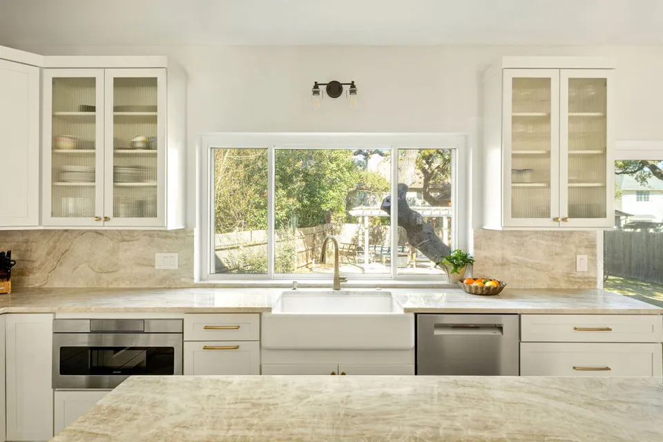 Farmhouse sink below a window, flanked by glass-front cabinets