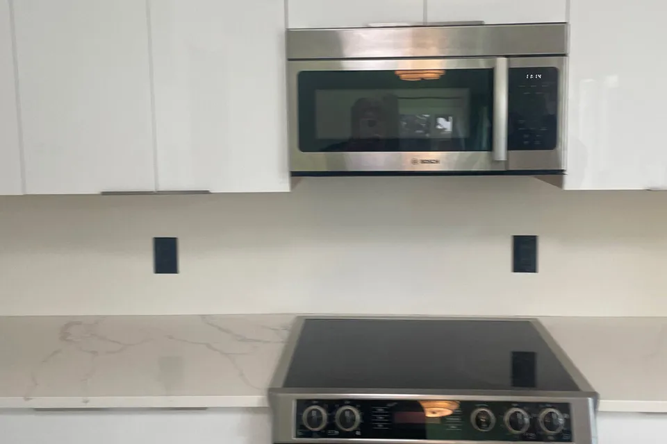 Kitchen before the remodel, with a glossy white backsplash, an electric cooktop and a microwave above