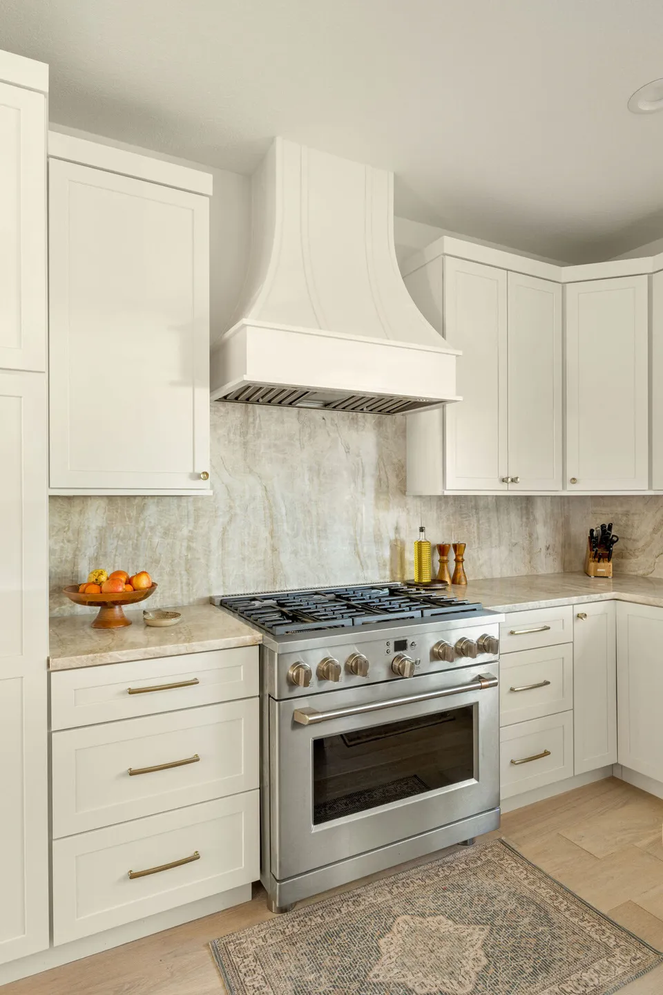 Stainless range below a cream plaster hood with a quartzite backsplash