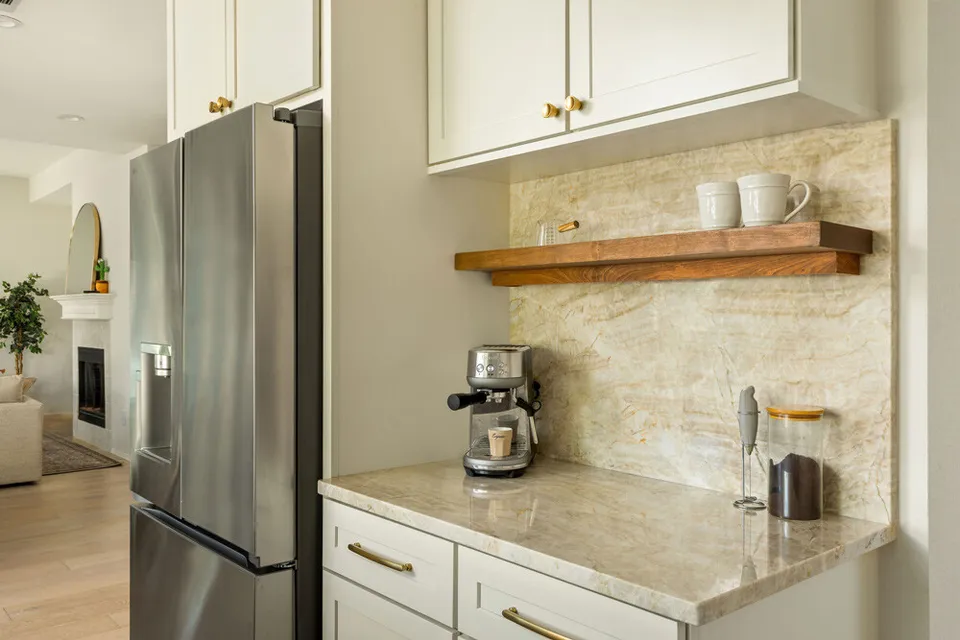 Stainless refrigerator beside a coffee station with a walnut floating shelf