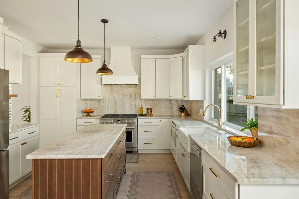 Walnut island with a quartzite top in a cream kitchen with black pendants