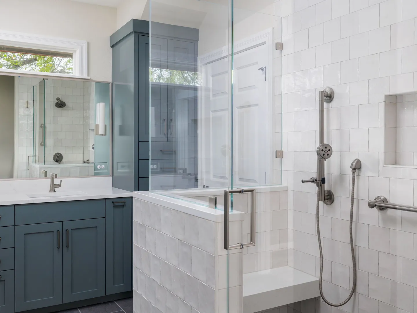 Glass shower with a handheld shower, a bench and grab bars beside a teal vanity