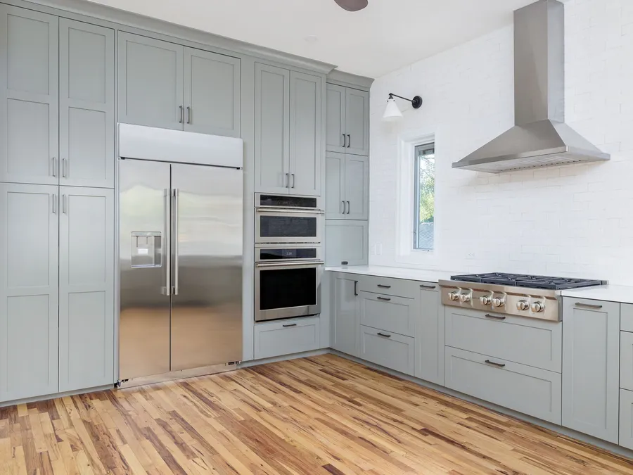 Grey shaker cabinets with a built-in refrigerator, wall ovens and a stainless chimney hood