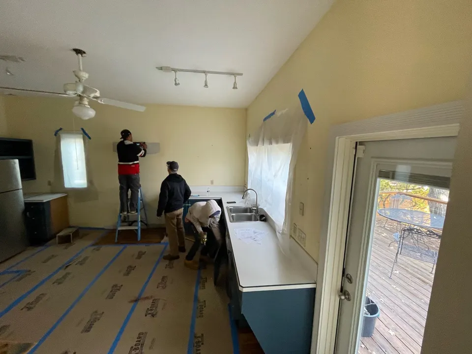 Kitchen during demolition, with workers, bare walls and protected floors