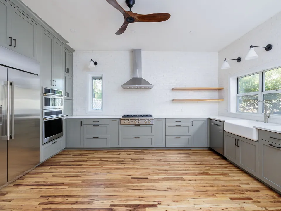 Kitchen after the remodel, with grey shaker cabinets, a stainless hood, open shelves and restored oak floors