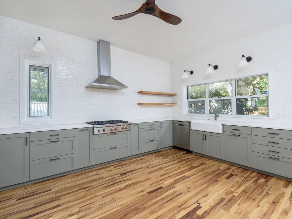 L-shaped kitchen with grey cabinets, white brick walls, open shelves and a farmhouse sink