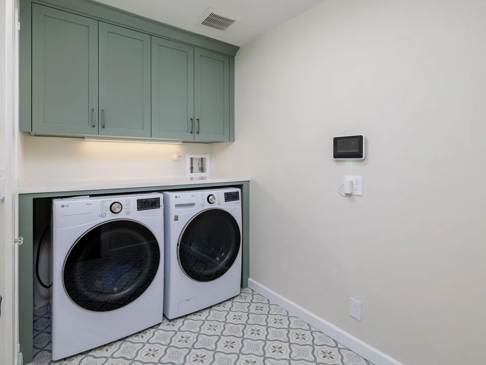 Laundry room with sage cabinets over a front-load washer and dryer on patterned tile