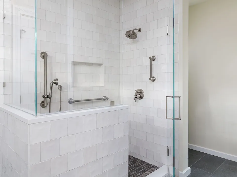 Walk-in shower with white square tile, a glass panel, a niche and grab bars