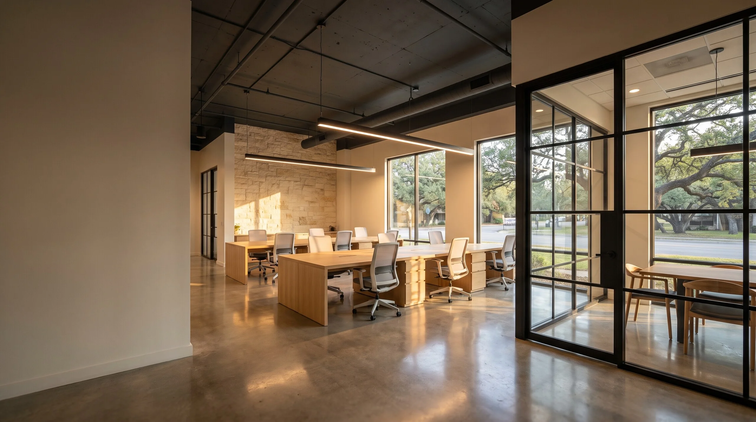 Open office with light wood desks, a limestone accent wall, polished concrete floors and a steel-framed glass meeting room